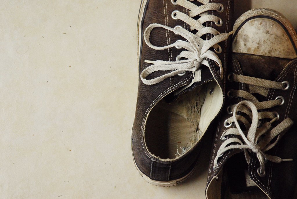 A worn pair of canvas high-top sneakers with dirty white toe caps and frayed laces